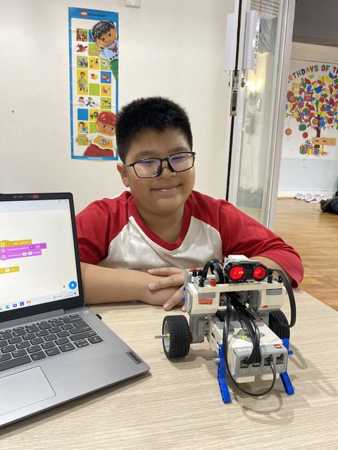 A student at a table with a laptop and the wheeled robot he programmed
