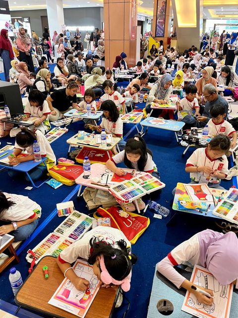 A hall full of children drawing and colouring at low tables during an art event