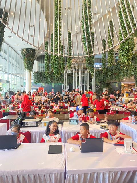 Rows of students in CK shirts working on laptops at an event in a large atrium